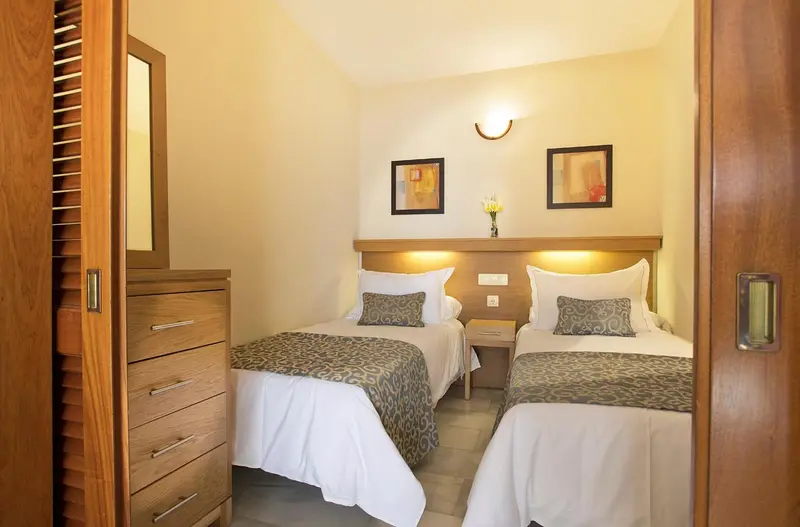 Une chambre lumineuse avec deux lits simples et une commode en bois.