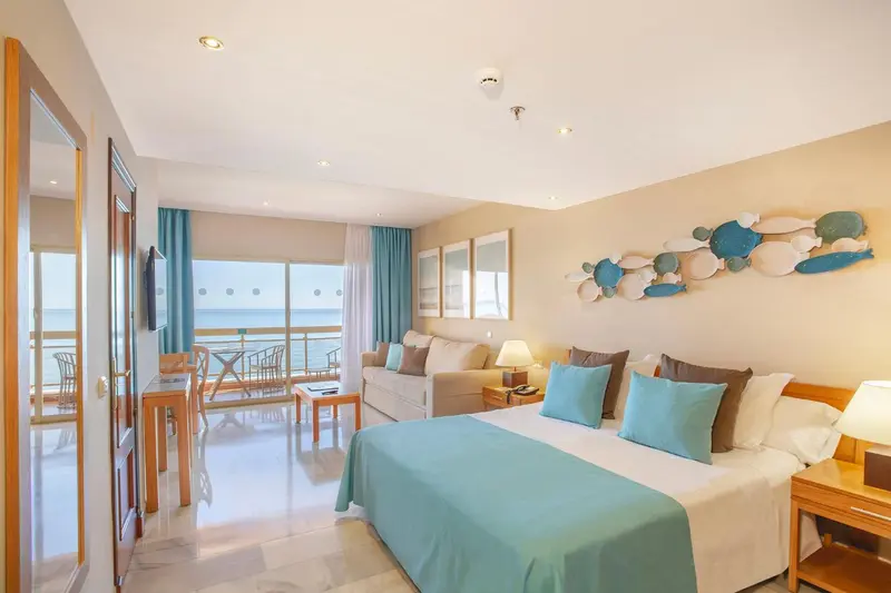 Une chambre lumineuse avec un lit et un coin salon donnant sur la mer.