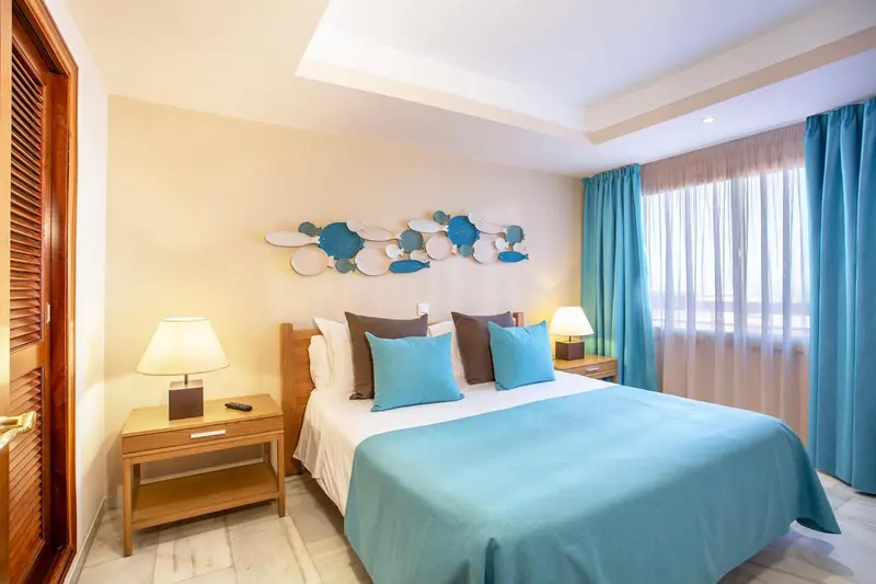Une chambre lumineuse avec un grand lit et des coussins turquoise.