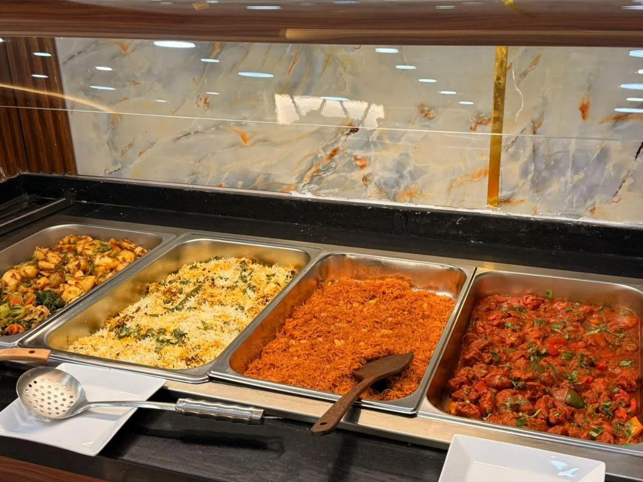 Un buffet propose une variété de plats chauds dans des bacs en acier inoxydable.