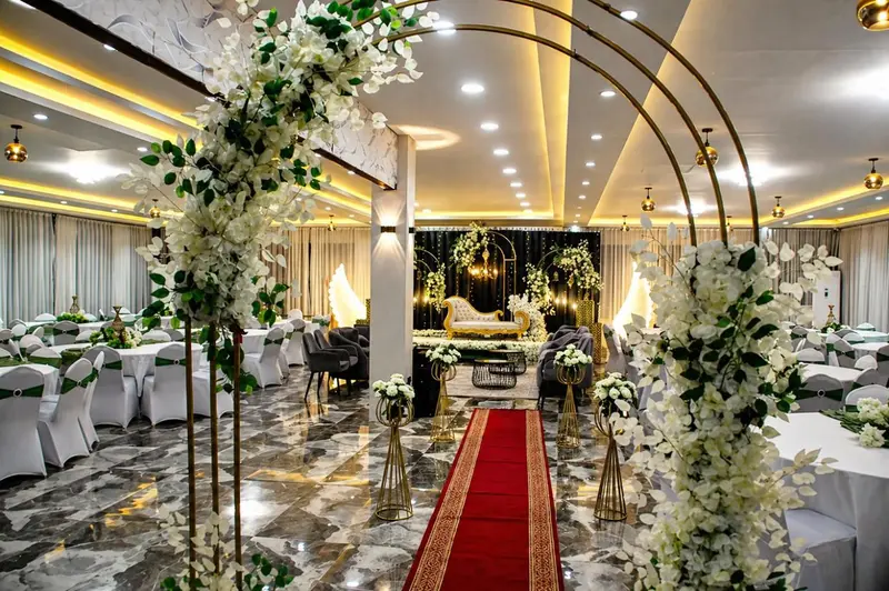 Une salle de réception décorée de fleurs et d'arches dorées accueille des tables dressées pour un événement.