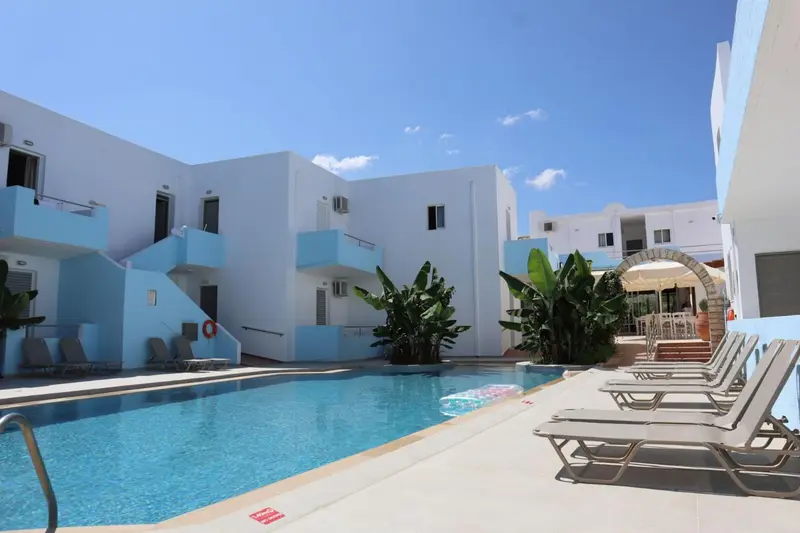Une piscine rectangulaire bordée de transats devant un bâtiment blanc à plusieurs niveaux.