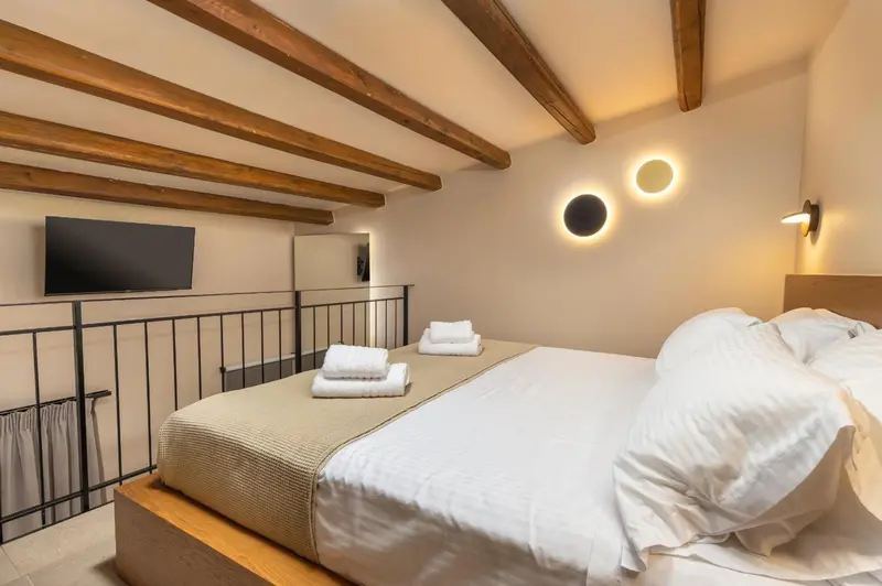 Une chambre lumineuse avec un lit double et des poutres apparentes au plafond.
