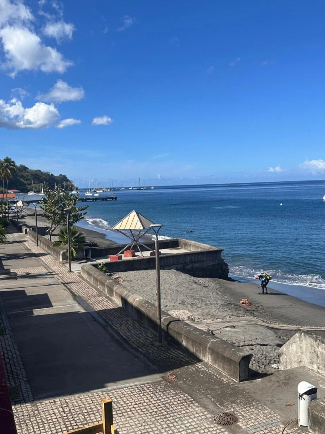 Vue d'une promenade en bord de mer avec une construction en pierre et des bateaux amarrés au loin.