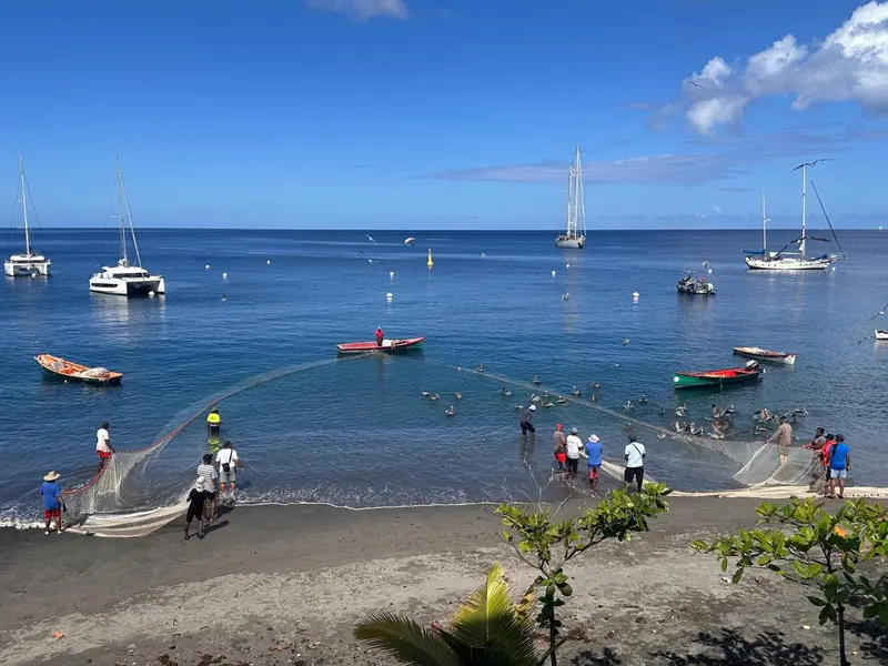 Une plage ensoleillée avec des bateaux à l'horizon et des pêcheurs tirant un filet.