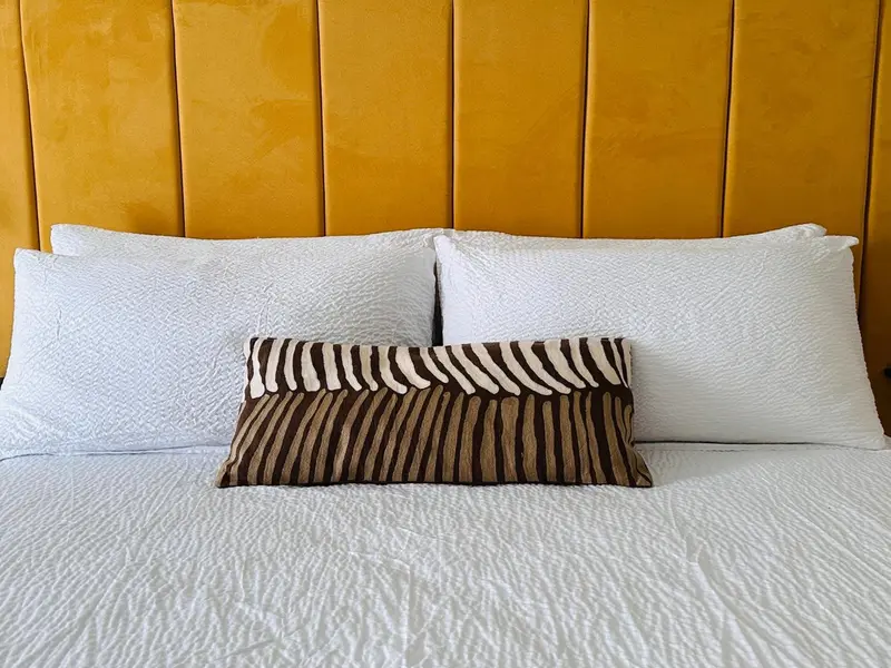 Un lit avec des oreillers blancs et un coussin à motifs zébrés est prêt pour le repos.