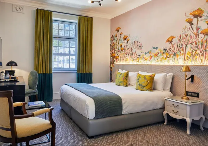 Une chambre lumineuse avec un lit recouvert d'une courtepointe blanche et de coussins colorés.