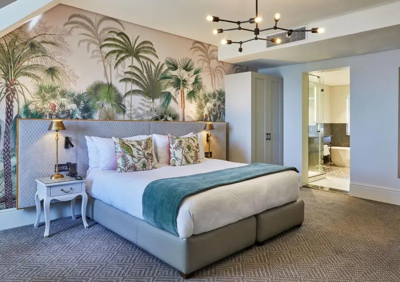 Une chambre lumineuse avec un grand lit et un mur décoré de motifs tropicaux.