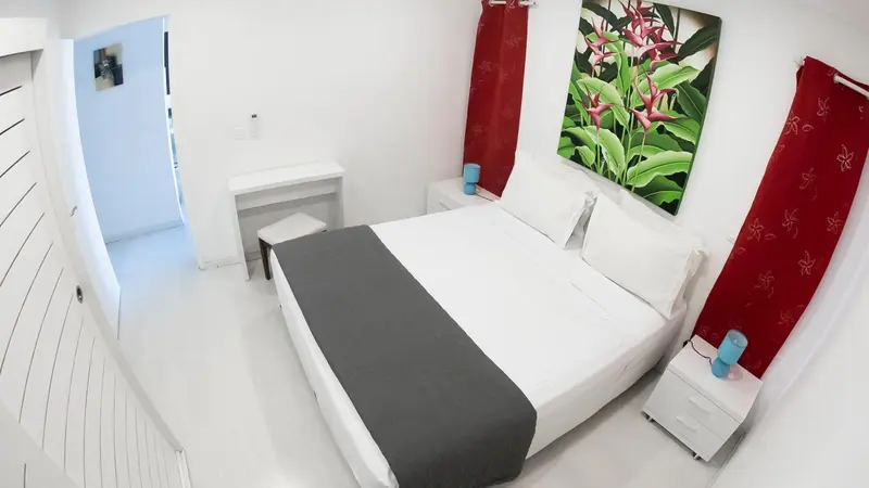 Une chambre lumineuse avec un grand lit recouvert d'une courtepointe grise.
