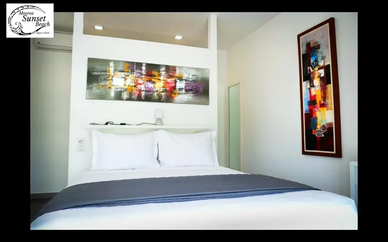Une chambre avec un grand lit recouvert d'une courtepointe grise et de coussins blancs, décorée d'un tableau abstrait.