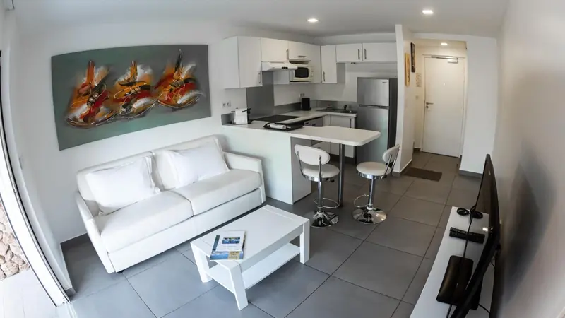 Espace de vie lumineux avec canapé blanc et cuisine équipée.