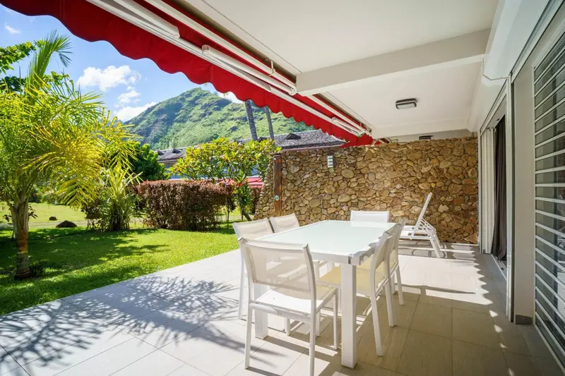 Terrasse ombragée avec table et chaises donnant sur un jardin soigné.