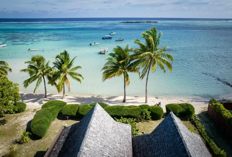 Vue aérienne d'une plage de sable blanc bordée de palmiers et de bateaux.