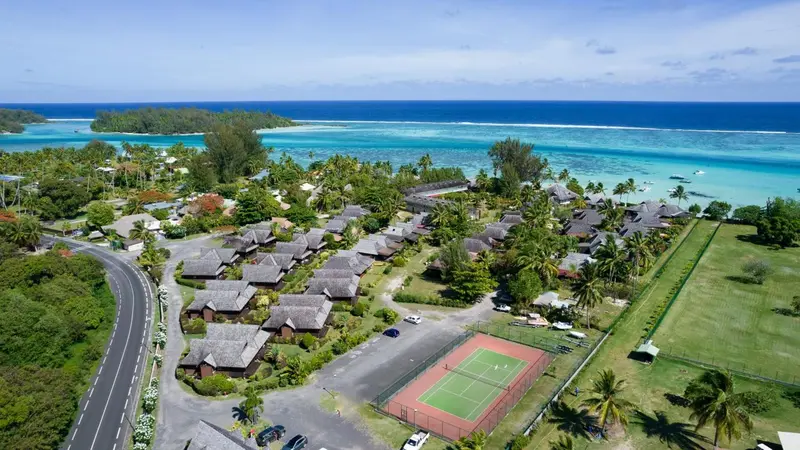 Vue aérienne d'un complexe hôtelier tropical avec des bungalows et un court de tennis.