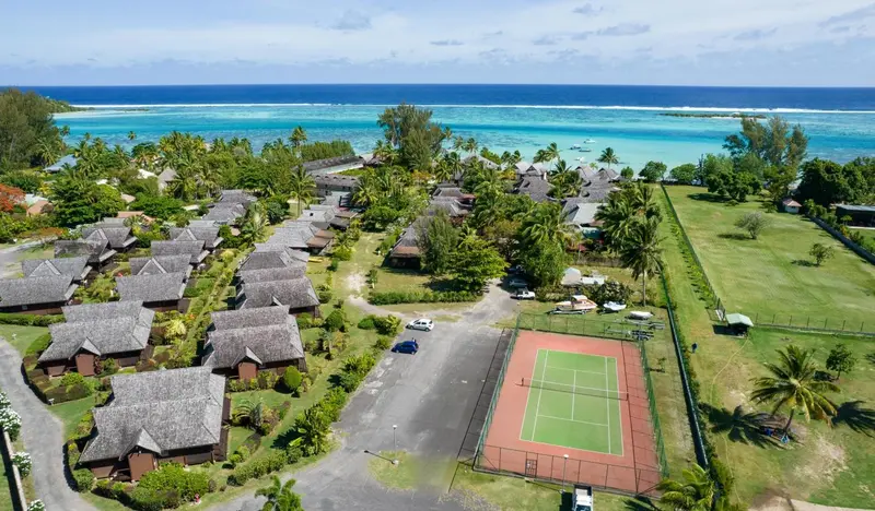 Vue aérienne d'un ensemble de bungalows avec un court de tennis et une végétation luxuriante.