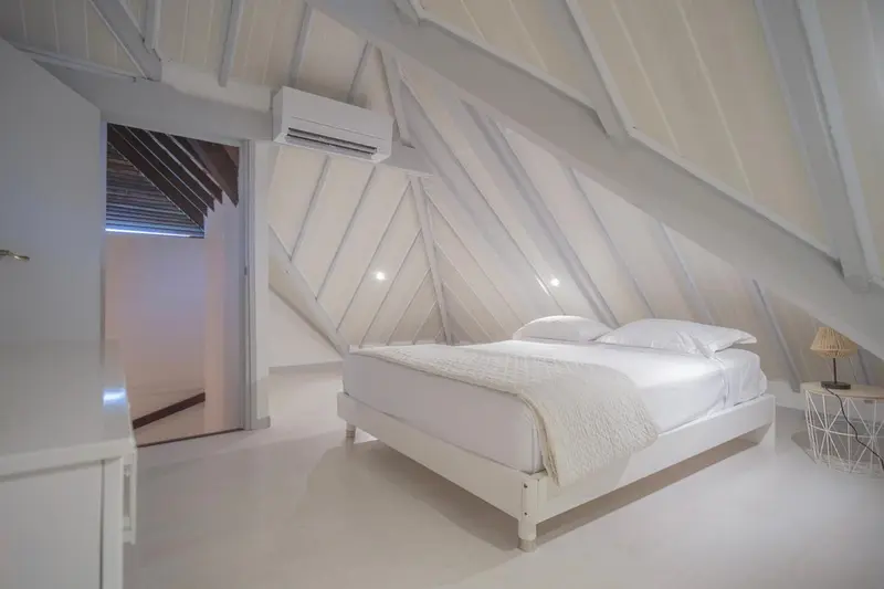Une chambre lumineuse avec un lit blanc et des murs clairs.