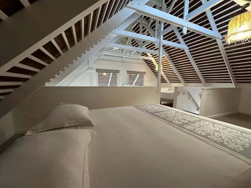 Une chambre mansardée lumineuse avec un lit recouvert d'une courtepointe décorative.