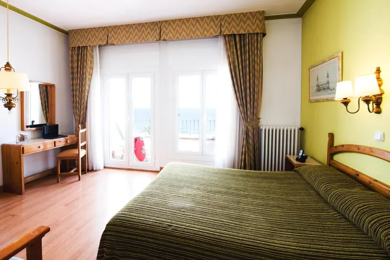 Une chambre lumineuse avec un lit et un bureau près d'une fenêtre donnant sur la mer.
