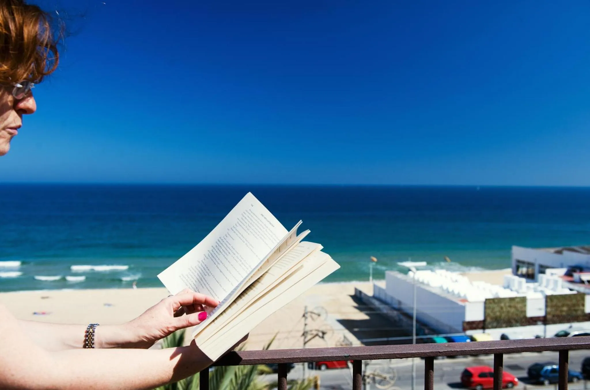 Une personne lit un livre sur une terrasse avec vue sur la mer.