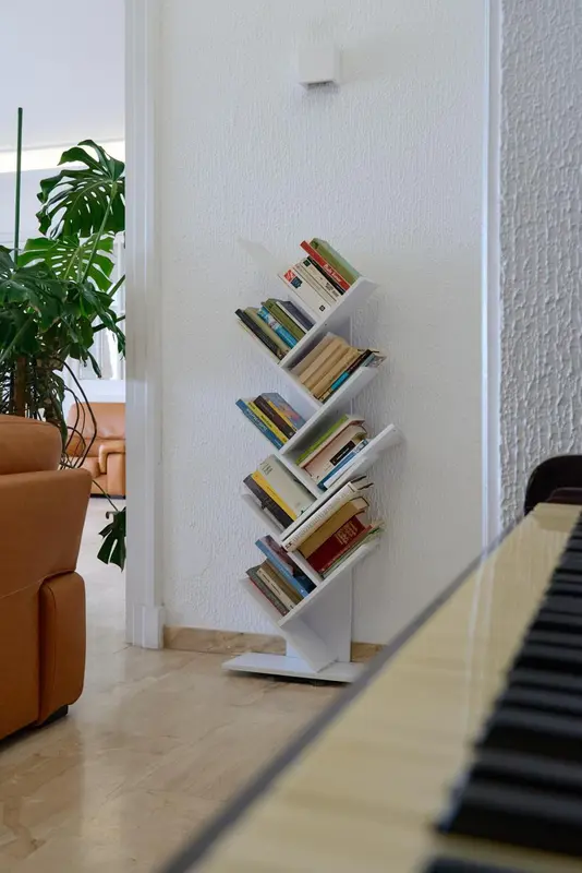 Une bibliothèque en forme d'arbre blanc est placée dans un coin d'une pièce lumineuse.