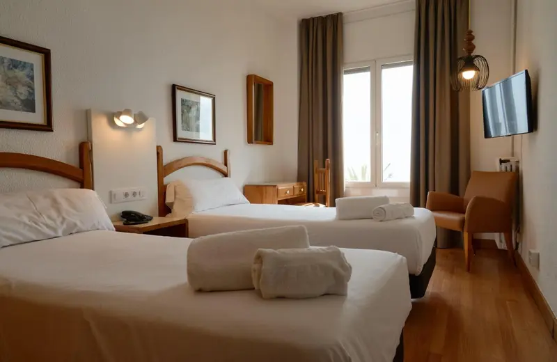 Une chambre lumineuse avec deux lits simples et un fauteuil.