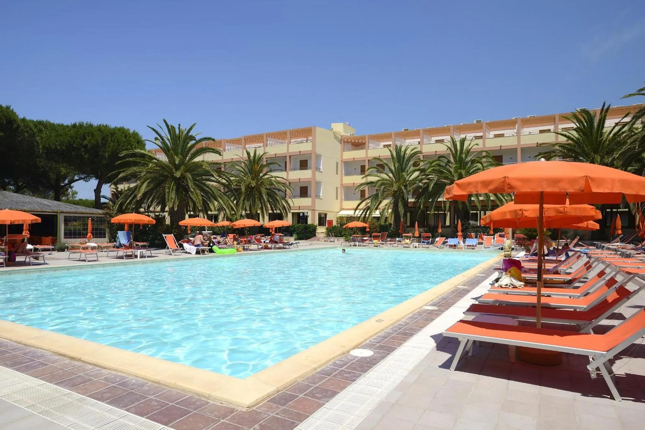Une piscine bordée de transats sous des parasols orangés devant un bâtiment à l'architecture claire.