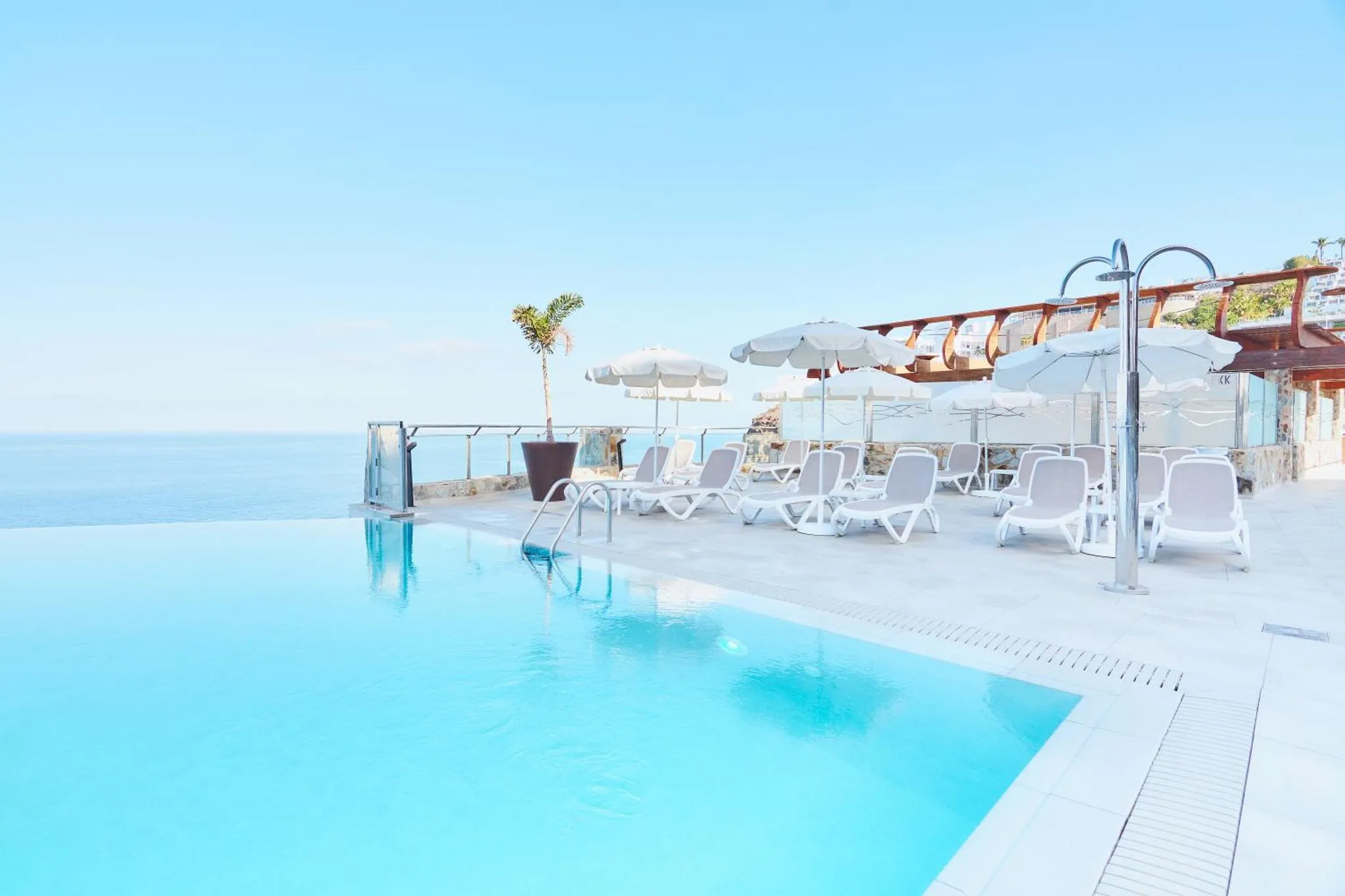 Transats blancs disposés autour d'une piscine à débordement avec vue sur la mer.