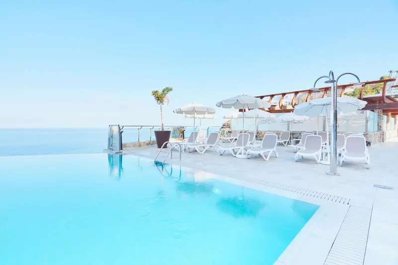 Transats blancs disposés autour d'une piscine à débordement avec vue sur la mer.
