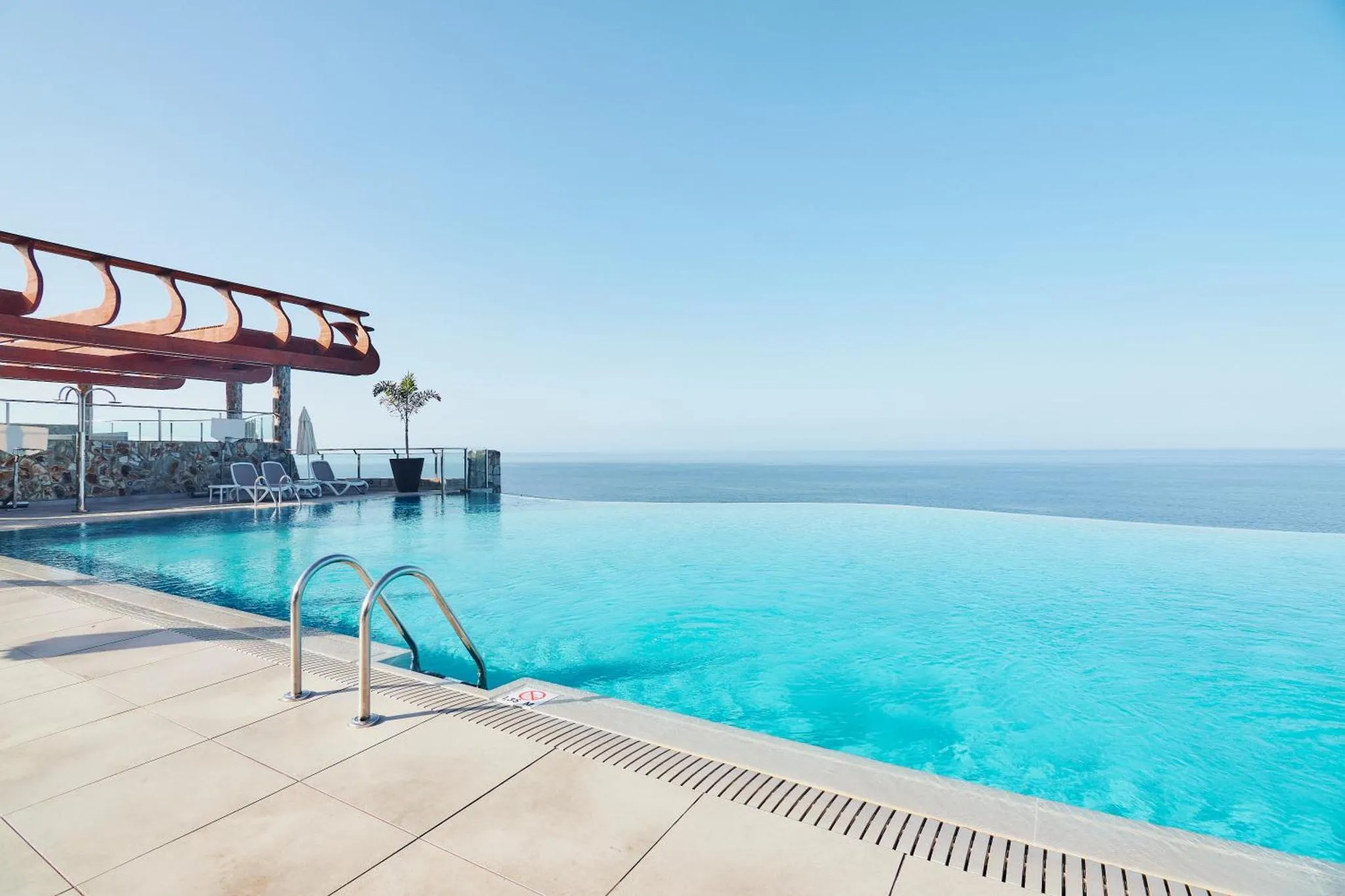 Piscine à débordement avec vue sur la mer et transats.