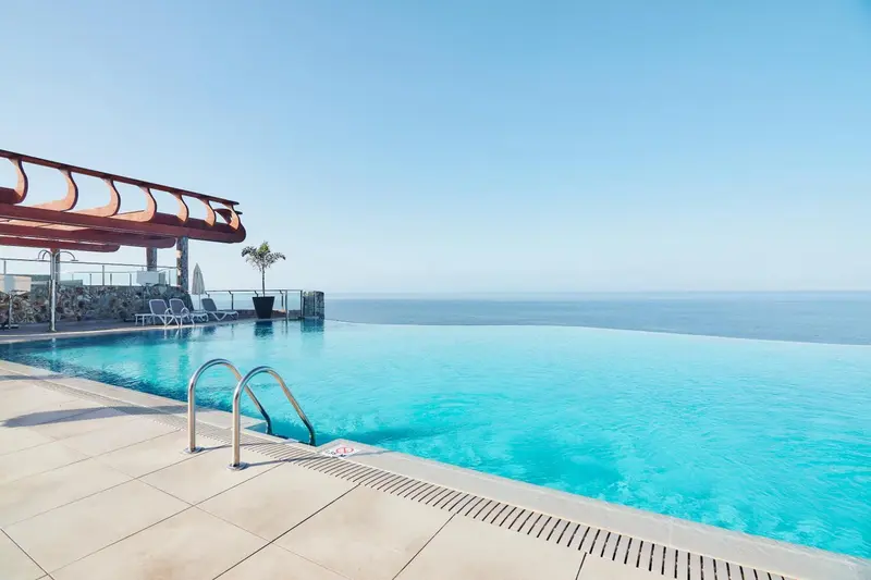 Piscine à débordement avec vue sur la mer et transats.