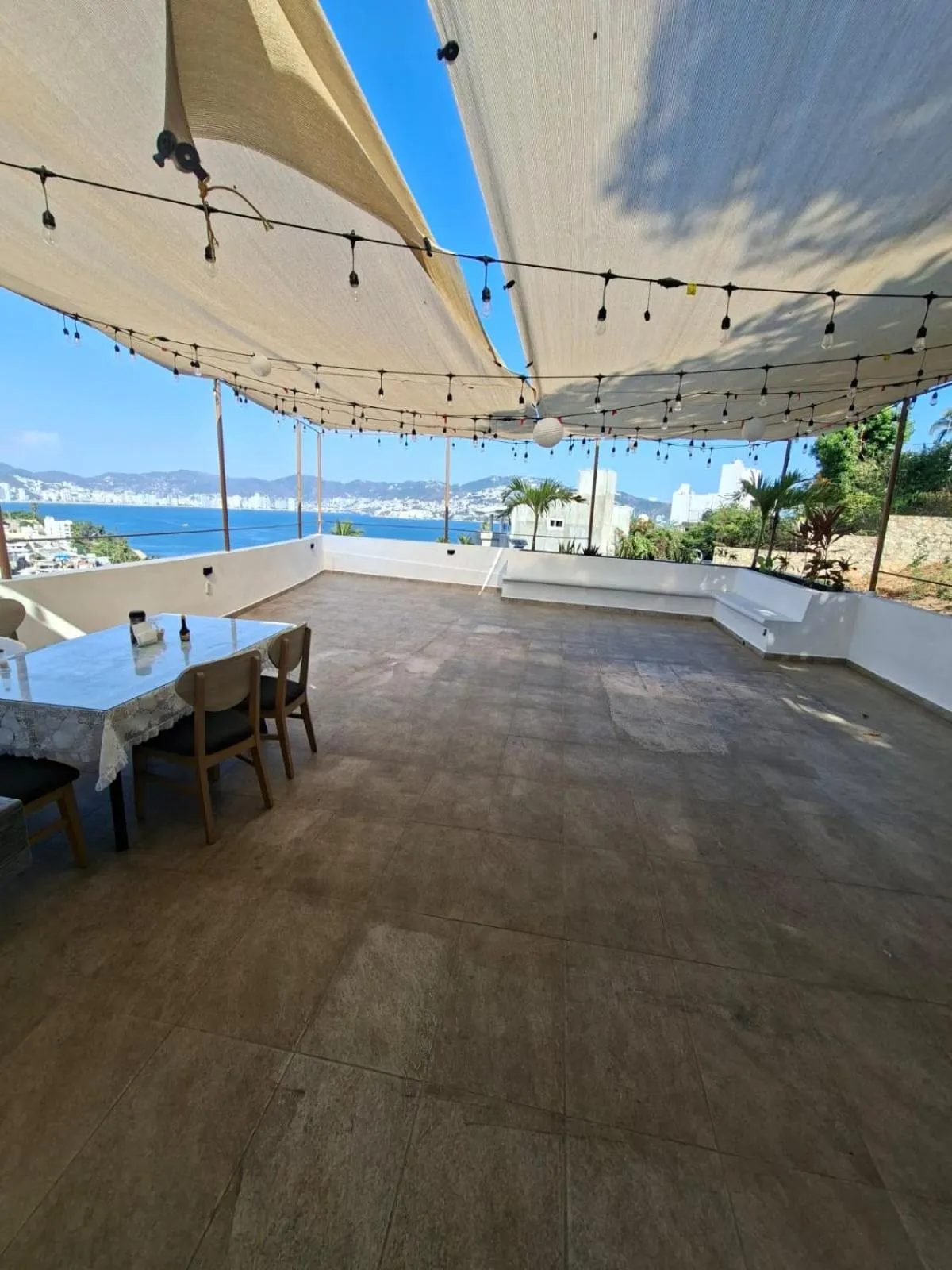 Terrasse ombragée avec tables et vue sur la mer.