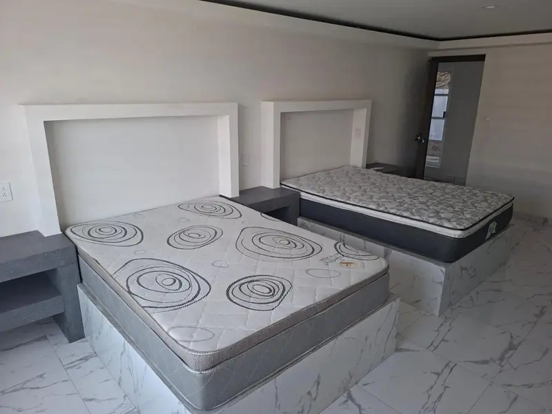 Deux lits doubles avec matelas décorés dans une chambre lumineuse.