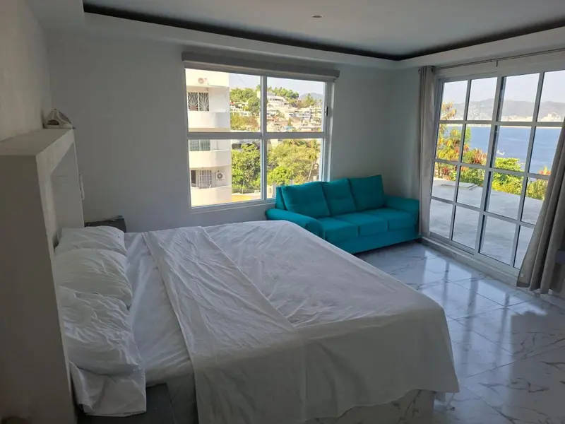 Chambre lumineuse avec un canapé bleu et une vue sur la mer.