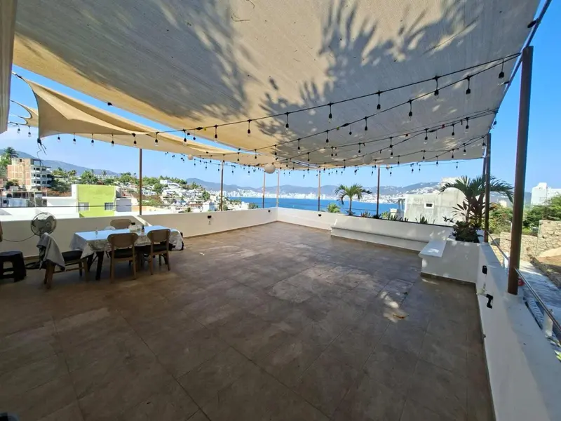 Terrasse ombragée avec table et chaises donnant sur la mer.