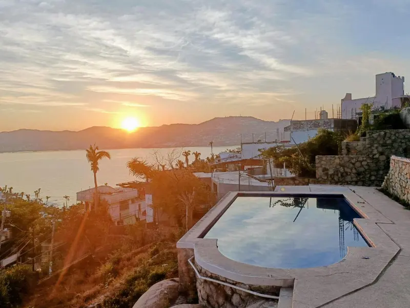 Une piscine au bord d'une falaise surplombe la mer au coucher du soleil.