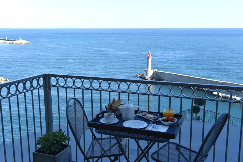 Une table avec un petit-déjeuner est posée sur un balcon avec vue sur la mer et un phare.