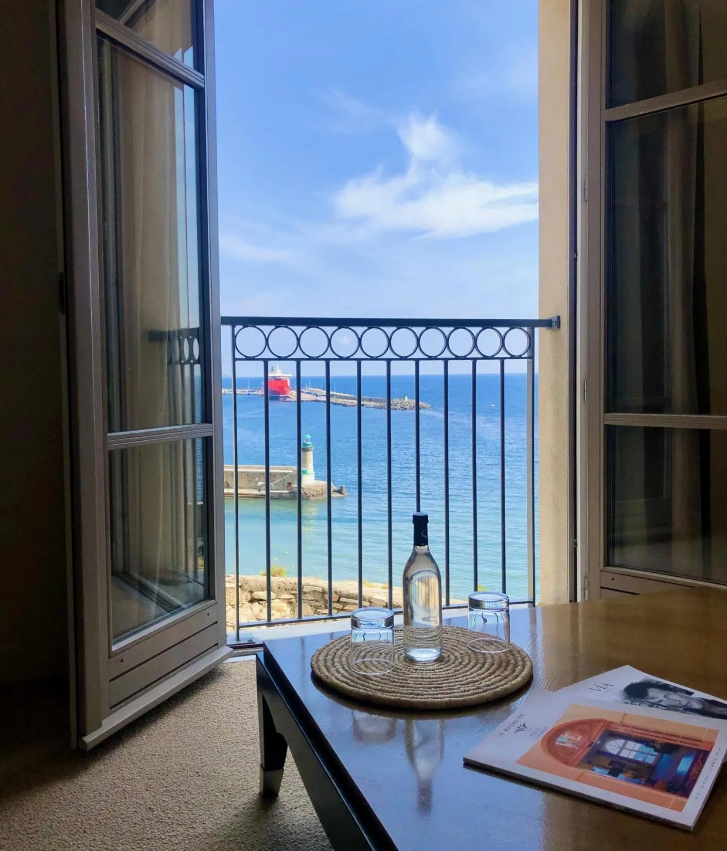Vue sur la mer depuis une chambre avec une bouteille et des verres sur une table.