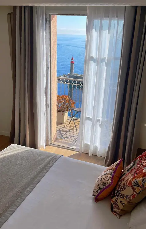 Une chambre lumineuse s'ouvre sur une vue mer avec un phare.
