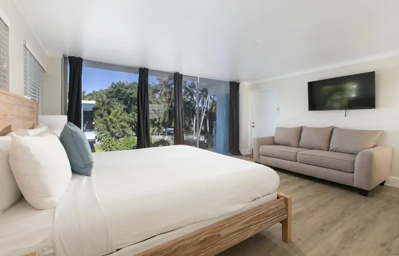 Une chambre lumineuse avec un grand lit et un canapé face à une baie vitrée.