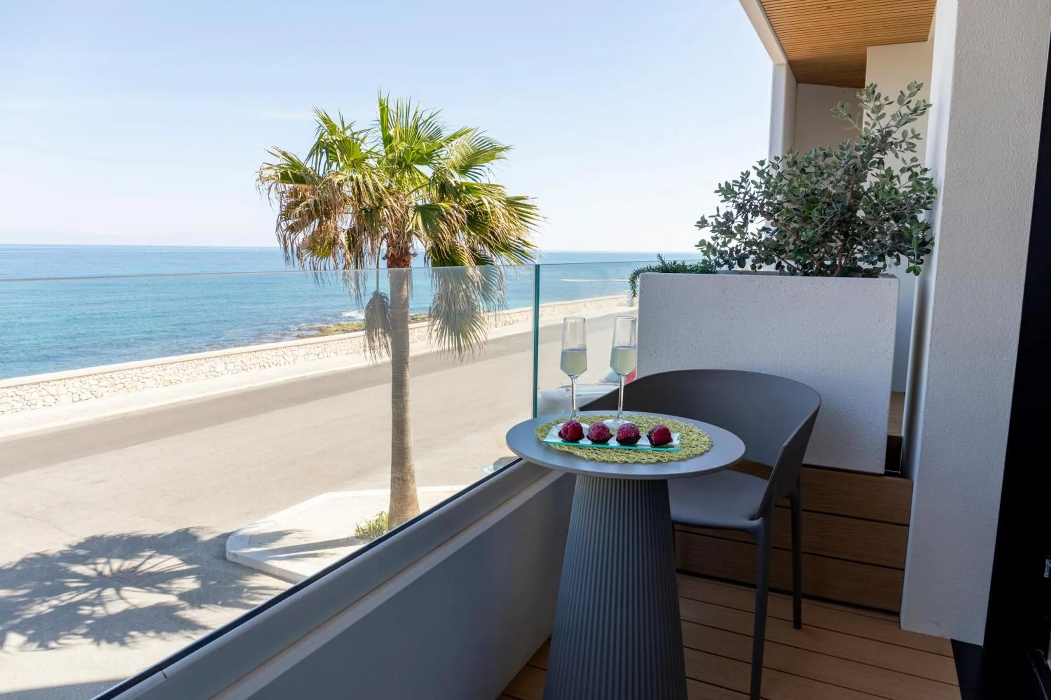 Une table ronde avec des verres et des fruits rouges sur un balcon avec vue sur la mer.