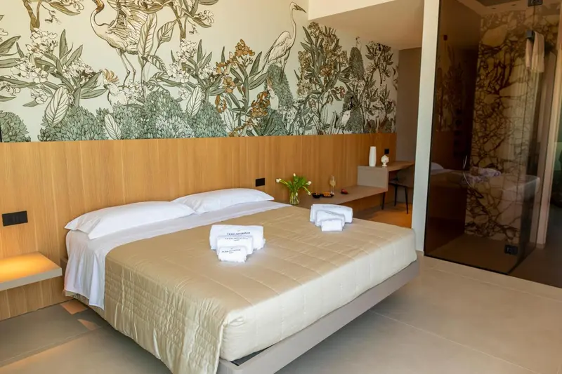 Une chambre lumineuse avec un grand lit et un mur décoré de motifs végétaux.