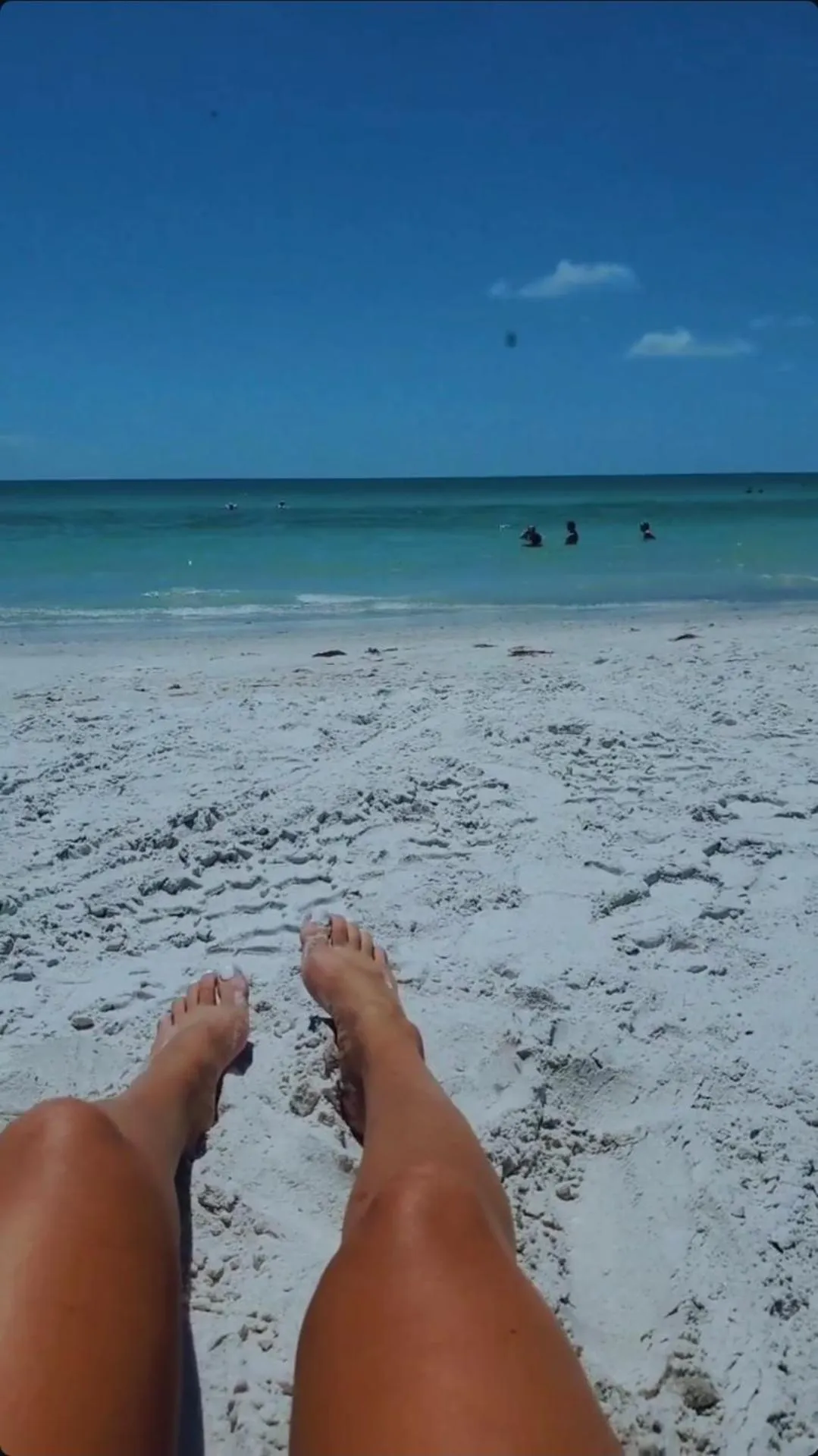 Pieds dans le sable blanc sur une plage ensoleillée face à une mer turquoise.