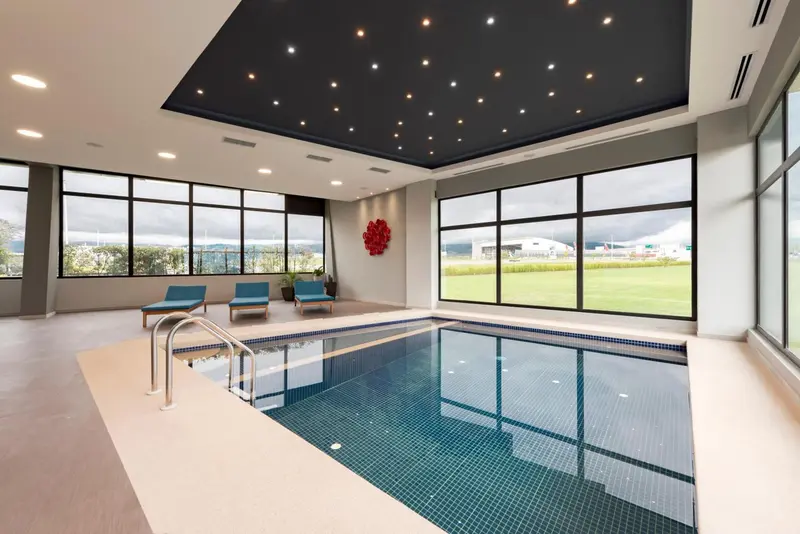 Une piscine intérieure lumineuse avec des chaises longues et de grandes baies vitrées.