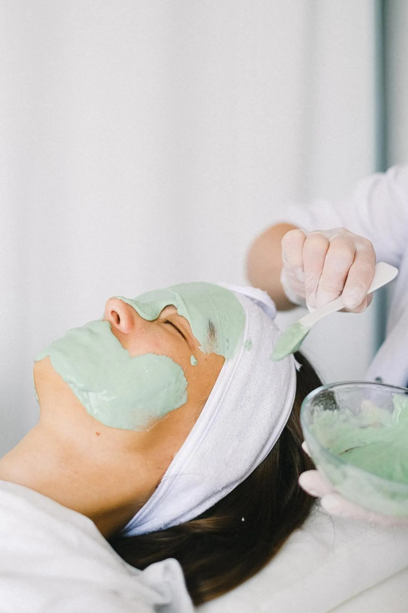 Une personne allongée reçoit un soin du visage avec une crème verte.