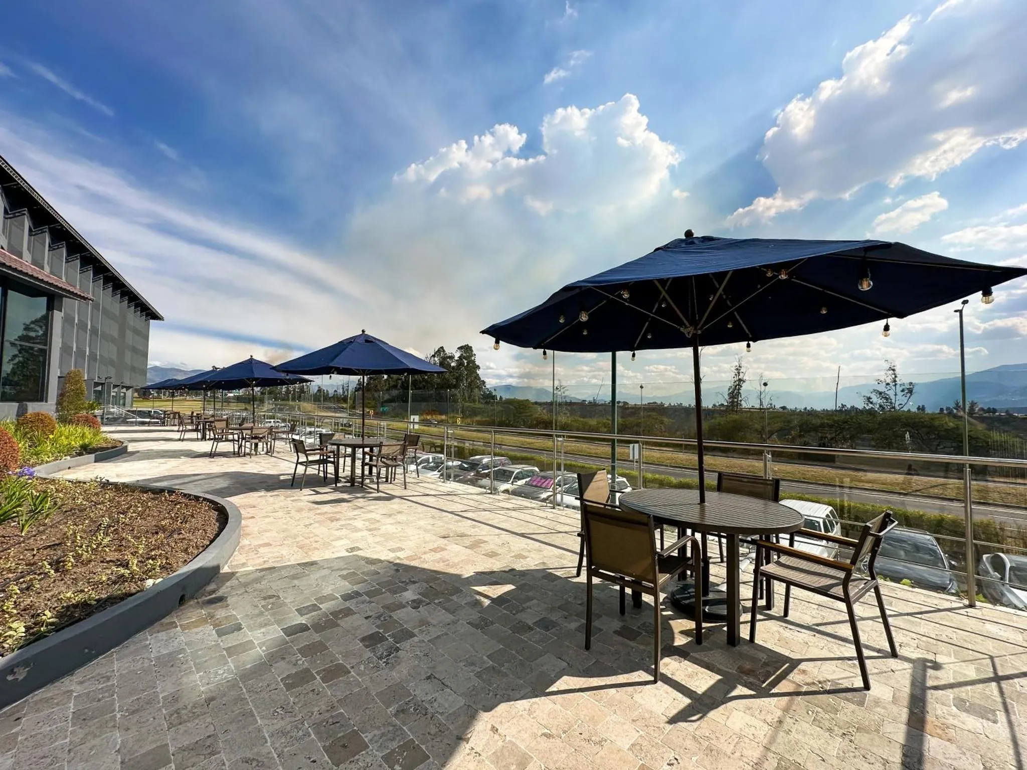 Terrasse ombragée avec tables et chaises offrant une vue sur un paysage vallonné.