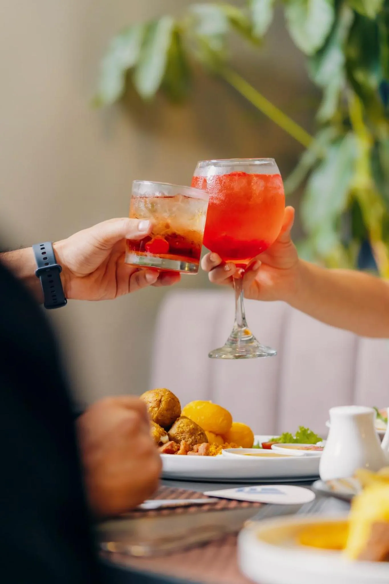 Deux personnes trinquent avec des verres colorés devant une assiette de nourriture.