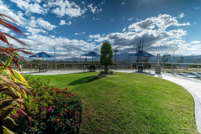 Terrasse verdoyante avec parasols bleus et vue sur les montagnes.