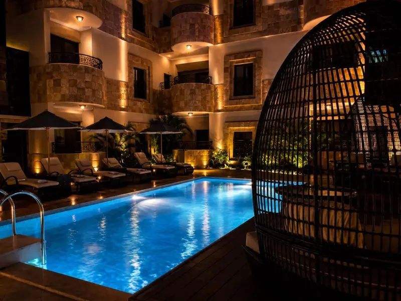 Piscine illuminée avec chaises longues et structure en osier.