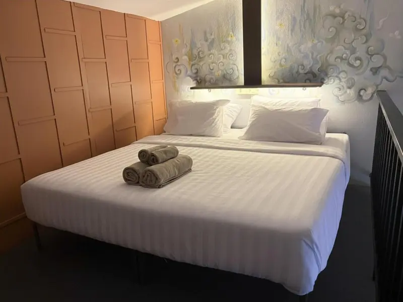 Une chambre lumineuse avec un grand lit recouvert de draps blancs et de serviettes roulées.