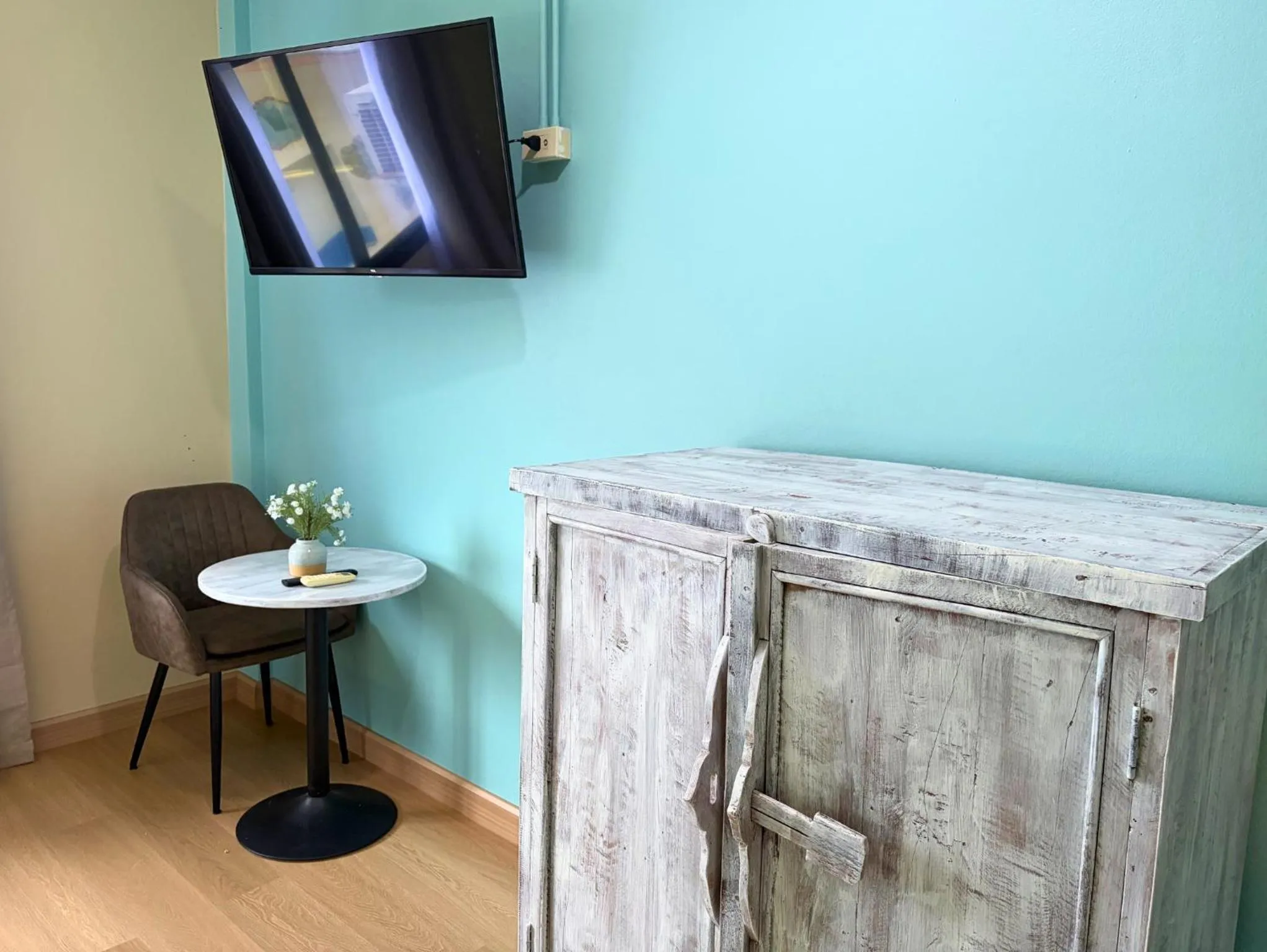 Une télévision murale surplombe une commode et une chaise dans une pièce lumineuse.
